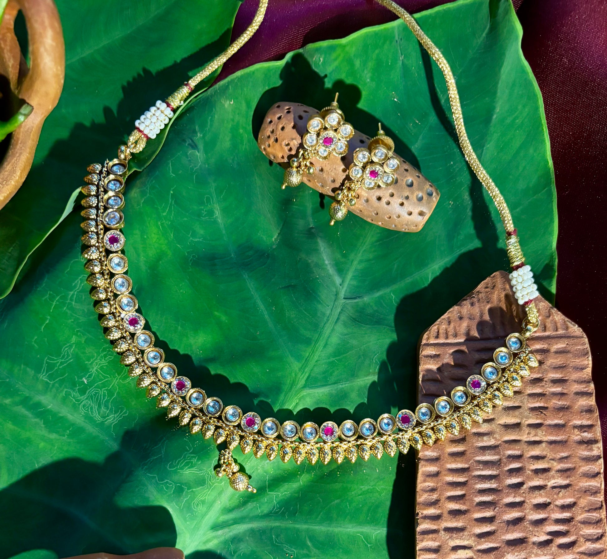 Maya Antique Gold Kundan Necklace with Ruby Accents and Matching Floral Stud Earrings on Green Leaf,Maya Antique Gold Kundan & Ruby Necklace Set | Traditional Jewellery.