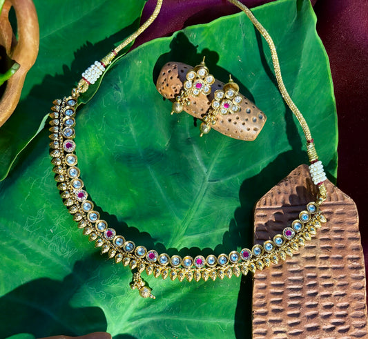 Maya Antique Gold Kundan Necklace with Ruby Accents and Matching Floral Stud Earrings on Green Leaf,Maya Antique Gold Kundan & Ruby Necklace Set | Traditional Jewellery.